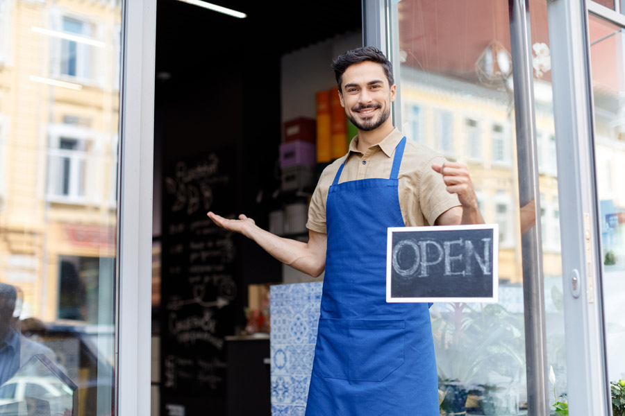 a business owner holding an open sign smiling with Business Insurance in Long Beach, CA, Seal Beach, CA, Huntington Beach, Lakewood, CA, Westminster, CA, Bellflower, CA